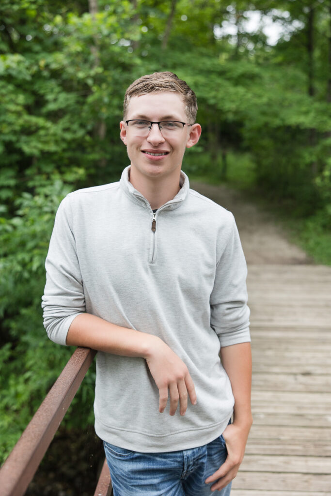senior guy standing on a bridge smiling at the camera