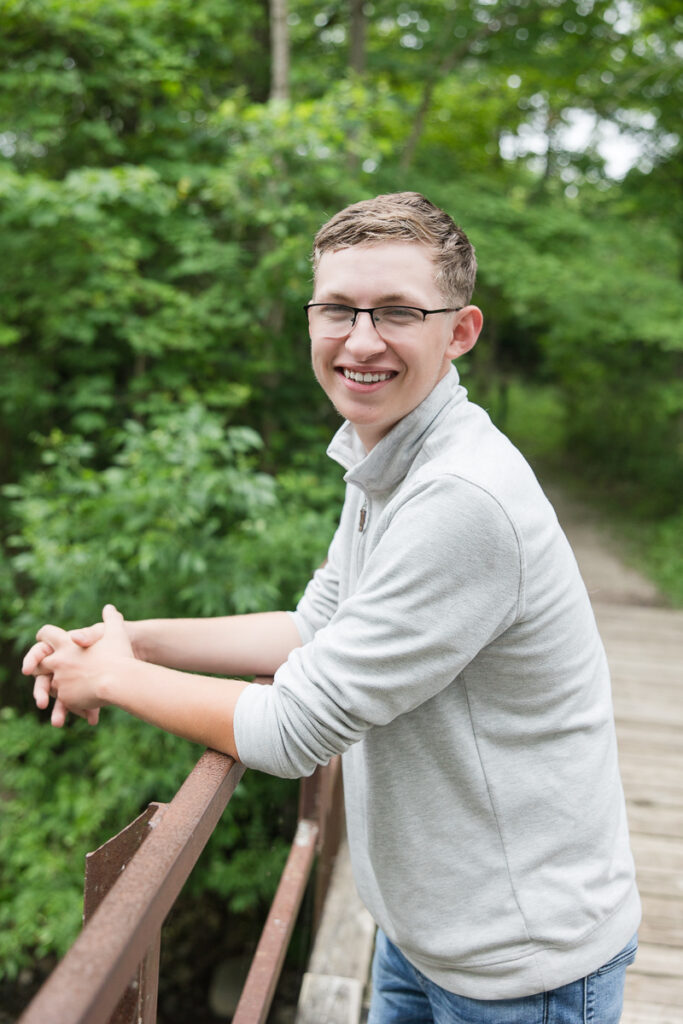 senior guy standing on a bridge smiling at the camera