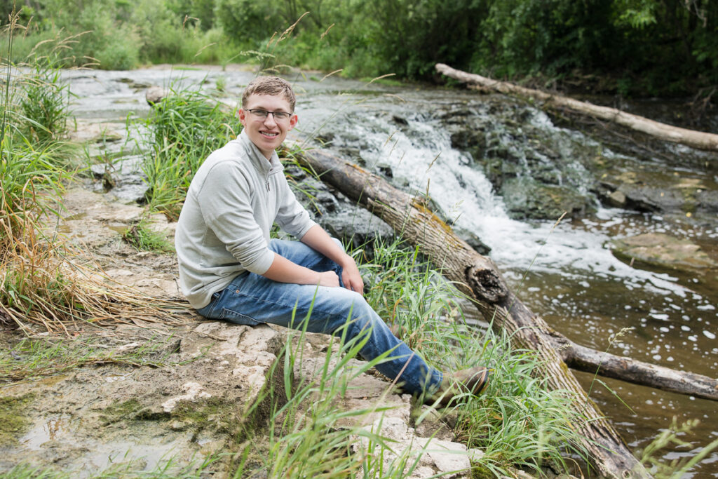 senior guy seated near a waterfall smiling at the camera