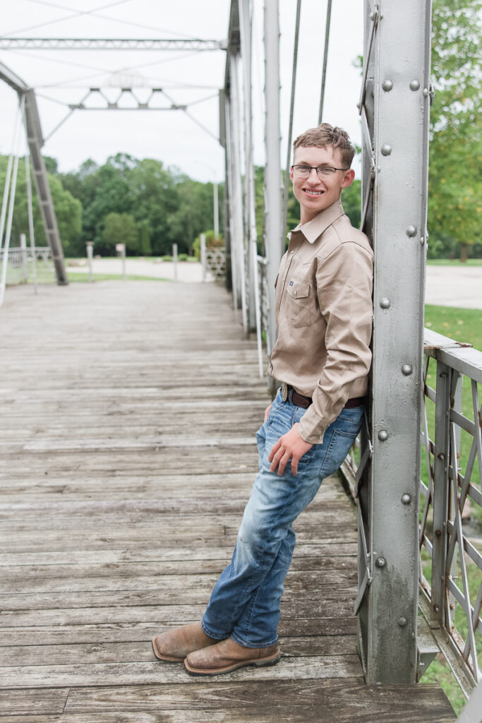 senior guy leaning against a pillar along a bridge smiling at the camera