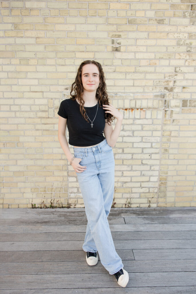 Senior girl standing in front of a creamy brick wall