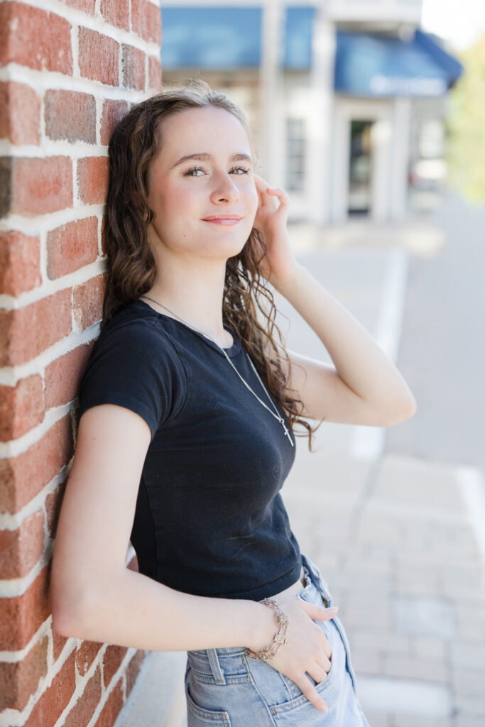 Senior portrait session of girl leaning against a red brick wall