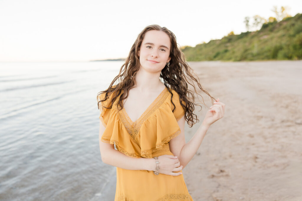 Senior portrait session in Port Washington, Wisconsin of girl standing on the beach playing with her hair