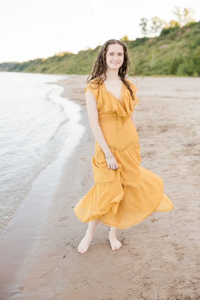 Senior portrait session in Port Washington, Wisconsin of girl standing on a beach smiling at the camera