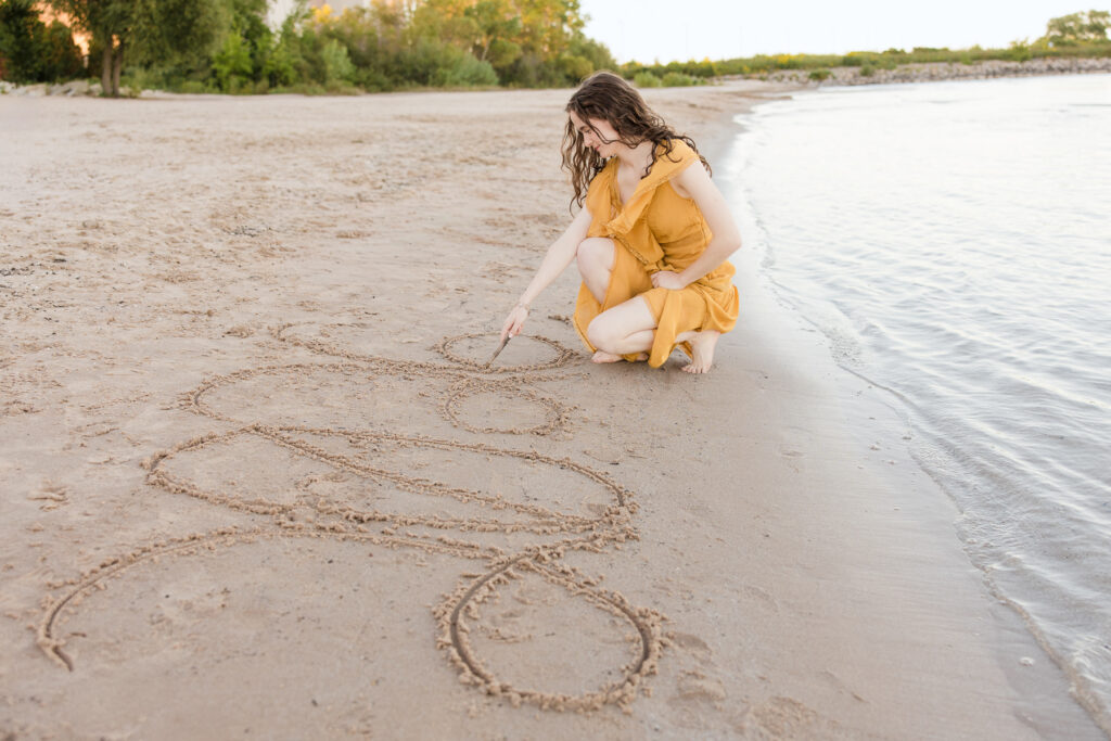 Senior girl writing "2026" in the sand