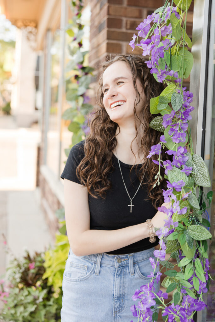 Senior portrait session in Port Washington, Wisconsin of girl standing next to flowers and laughing